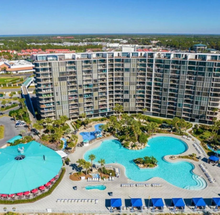 Aerial view of Edgewater Resort featuring lagoon-style swimming pools, palm trees, and beachfront resort buildings on a sunny day.