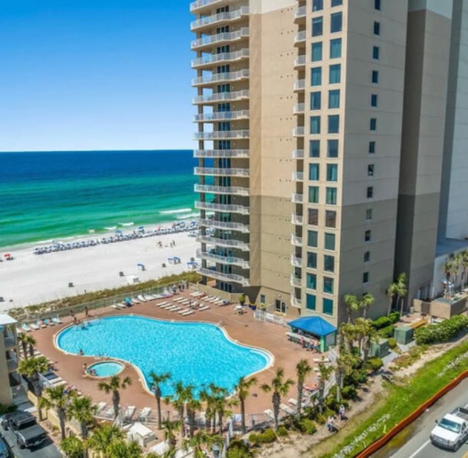 Aerial view of an oceanfront condominium with a large beachfront pool, direct beach access, and high-rise buildings overlooking the Gulf shoreline.
