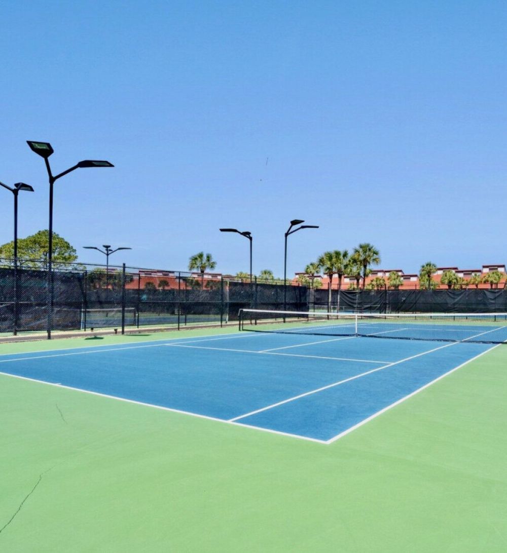 Outdoor tennis courts at Edgewater Beach Resort featuring multiple lighted courts and palm-lined surroundings in Panama City Beach.