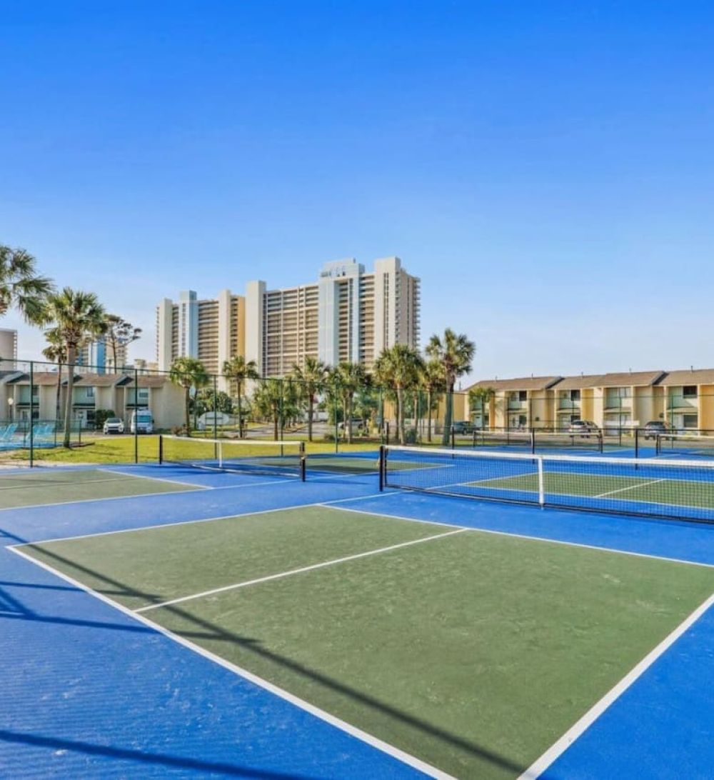 Pickleball and tennis courts at Gulf Highlands Beach Resort with townhomes and high-rise buildings in the background.