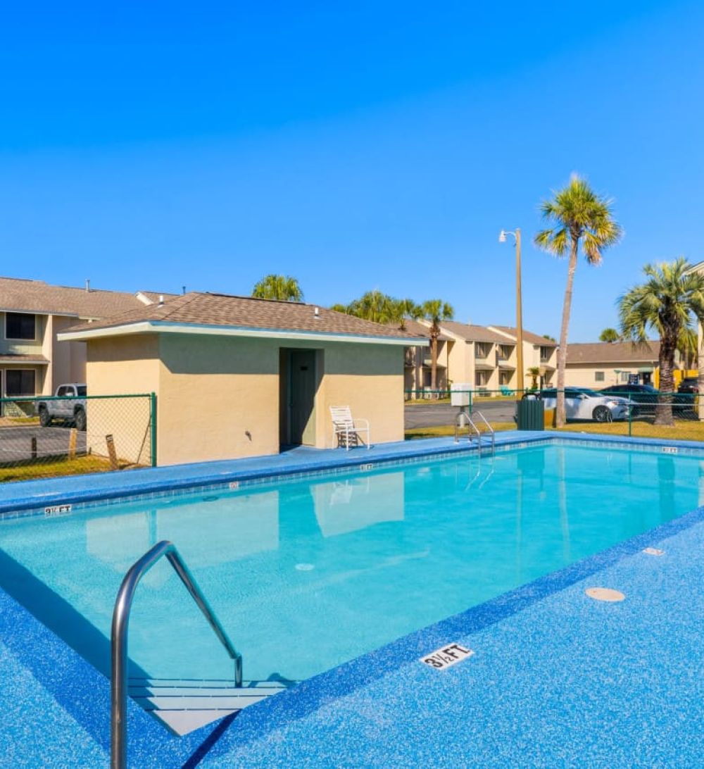 Outdoor community pool at Gulf Highlands Beach Resort with townhome units and palm trees around the deck area.