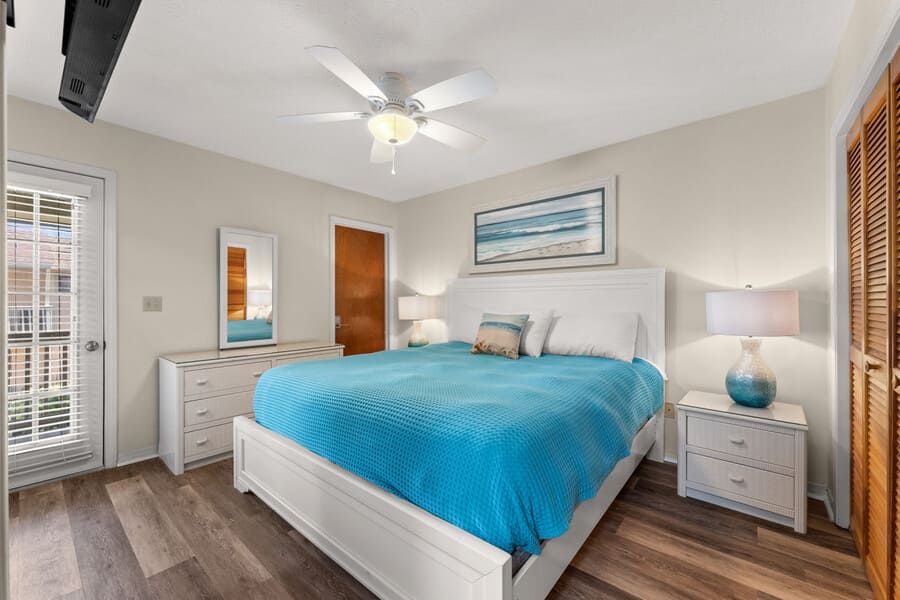 Primary bedroom at Gulf Highlands Beach Resort with a king bed, ceiling fan, white furniture, and private balcony access.