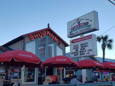 Exterior of Shuckums Oyster Pub & Seafood Grill with red umbrellas, casual patio seating, and marquee signage.