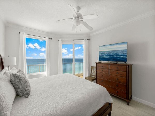 Primary bedroom at Grandview East Resort Condo featuring a king bed, TV, ceiling fan, and floor-to-ceiling windows with Gulf of Mexico views.