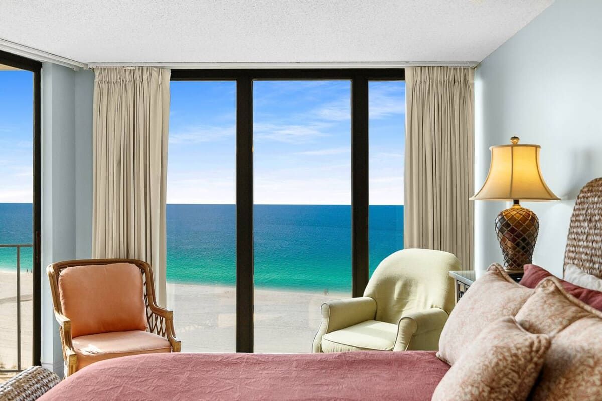 Oceanfront master bedroom in Edgewater Beach Resort with floor-to-ceiling windows showcasing emerald-green Gulf waters and white-sand shoreline.