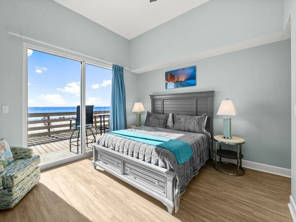 Ground-floor bedroom at Tidewater Beach Resort with a king bed and sliding doors leading to a private deck overlooking the beach.