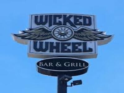 The Wicked Wheel Bar & Grill sign with winged logo against a clear blue sky in Panama City Beach.