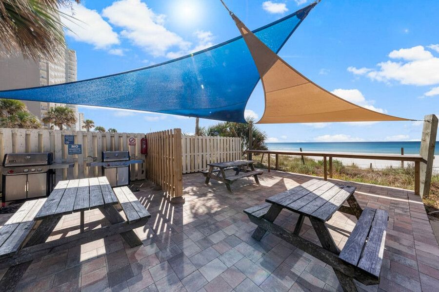 Beachfront grilling and picnic area at Grandview East Resort with shaded seating, outdoor grills, and Gulf of Mexico views.
