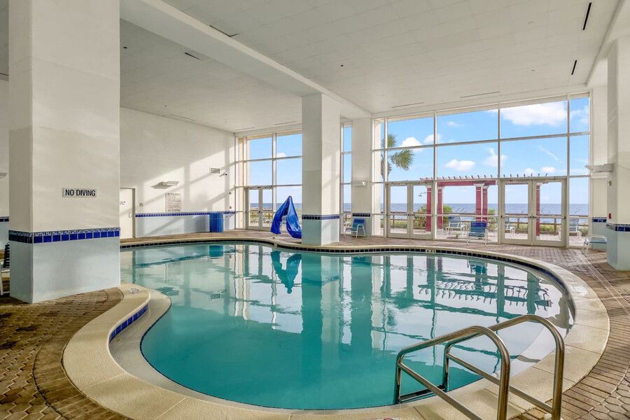 Indoor heated swimming pool with large windows and ocean views at a beachfront condominium.