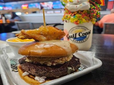 Gourmet burger topped with a chicken wing and a colorful specialty milkshake at Gulf Coast Burger Co. in Panama City Beach.