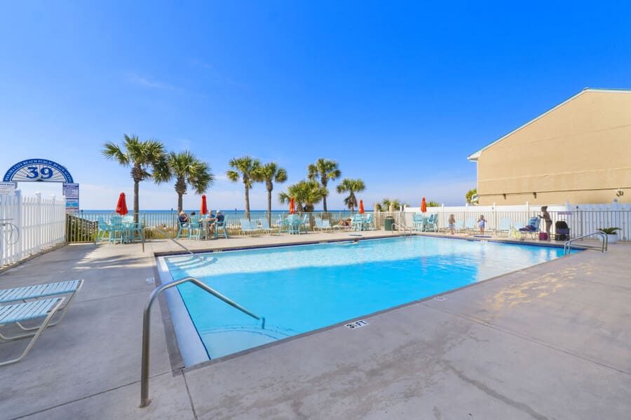 Outdoor beachfront pool at Gulf Highlands Beach Resort with lounge seating, palm trees, and views of the Gulf of Mexico.