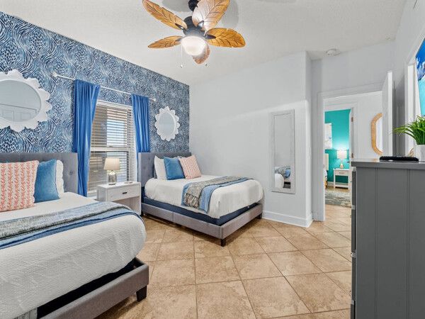 Guest bedroom featuring two full beds, patterned blue accent wall, and tropical ceiling fan at Ocean Ritz.