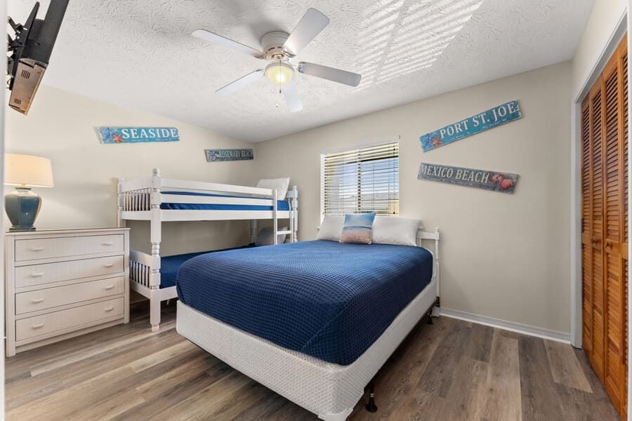 Guest bedroom at Gulf Highlands featuring a queen bed, bunk beds, coastal wall décor, and bright natural lighting.