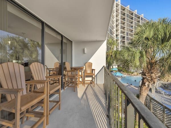 Private balcony at Edgewater Beach Resort with Adirondack seating and a relaxing pool view surrounded by palm trees in Panama City Beach.