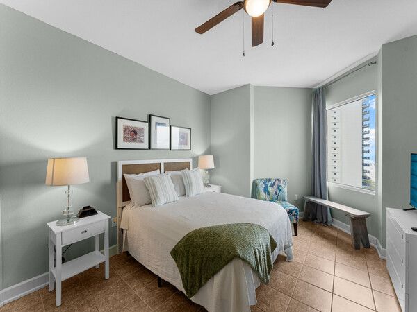 Bright bedroom at a Tidewater Beach Resort condo featuring a queen bed, coastal décor, ceiling fan, and natural light.
