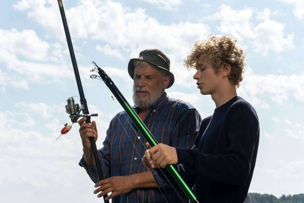 A grandfather and grandson bond while preparing fishing rods on a bright day outdoors.