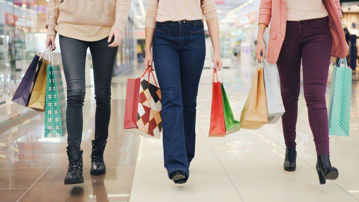 Three women walk with shopping bags in a mall.