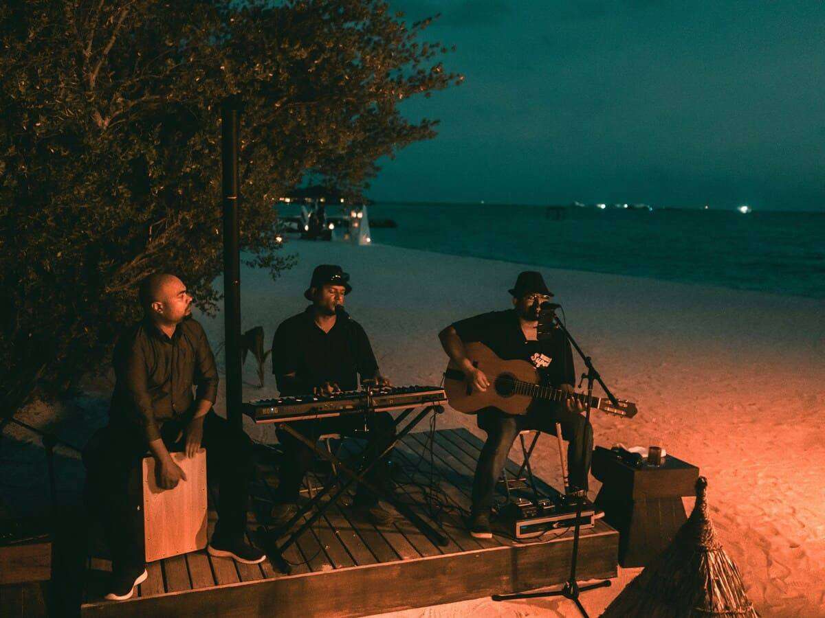 Three men playing musical instruments on a dock at the beach