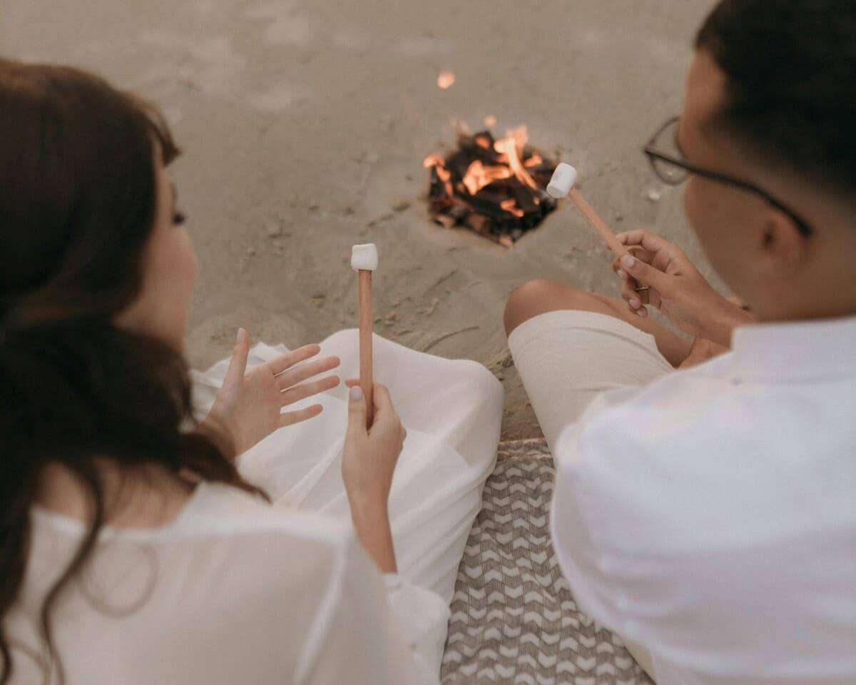 A couple roasting marshmallows over a beach bonfire, enjoying a cozy evening.